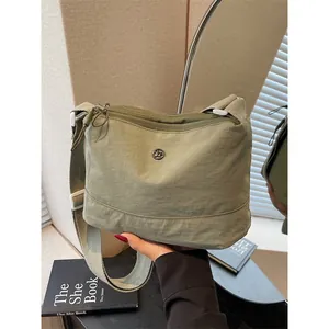 Olive green casual canvas crossbody bag with adjustable wide strap and round metal logo