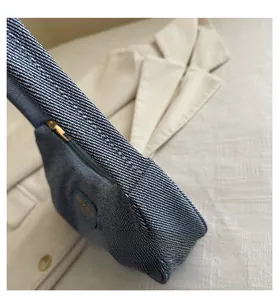 Detail of blue denim shoulder bag with textured fabric, gold zipper and romantic branding