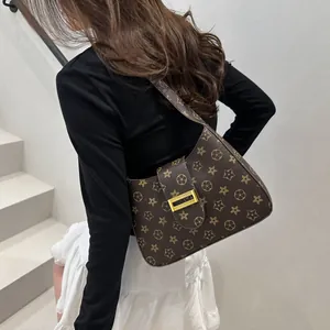 Borsa a spalla marrone con monogramma e chiusura dorata, indossata con stile da modella