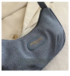 Detail of blue denim crescent bag featuring a woven texture and leather brand plaque