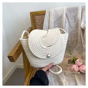 Détail du sac seau tissé blanc avec rabat en spirale et fermoir perle sur une chaise