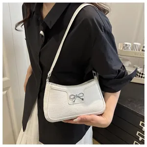 Close-up of white crocodile embossed shoulder bag with a silver metal bow detail