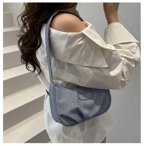 Close-up of blue denim underarm bag with pleated texture and oval logo on white shirt