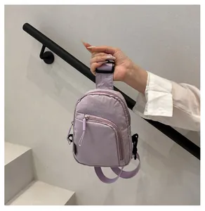 Detalle de riñonera de nailon morado claro con cremalleras y correa ajustable de hombro