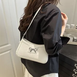 White faux crocodile shoulder bag with metallic bow detail shown on model's shoulder