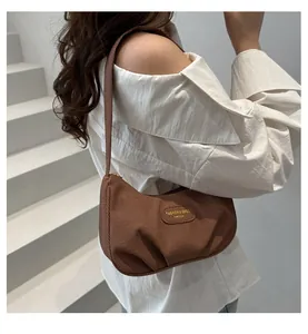 Detail of a brown textured canvas hobo bag with a fashion logo patch worn as an underarm bag