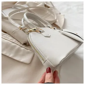 Detail of white faux leather shell bag with gold hardware on chic beige blazer