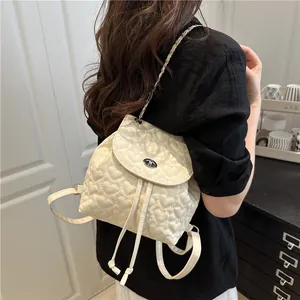 Cremefarbener Rucksack mit Herzsteppung, Drehverschluss und Kettenriemen am Modell
