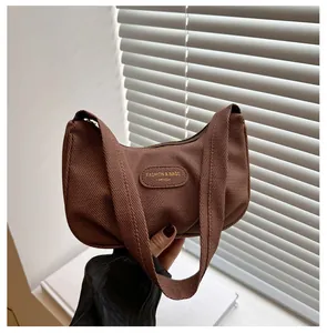 Detail of a brown textured canvas hobo bag featuring an oval leather patch and wide strap