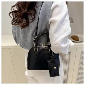 Detail of black faux leather shell bag with adjustable strap and mini charm pouch accessory