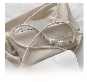 Detailed shot of white leather bag featuring thin knotted straps and silver metal buckle