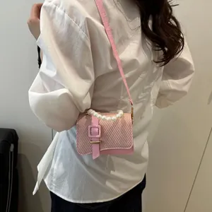 Pink woven mini crossbody bag with pearl handle and leather strap on a female model
