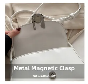 Detailed view of the hardware magnetic buckle on a white leather shoulder bag