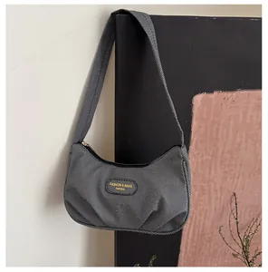 Detail showing grey denim texture and leather logo patch on pleated hobo shoulder bag
