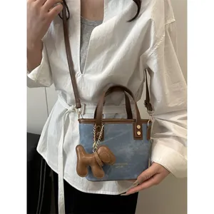 Retro denim bucket bag with brown leather trim and a cute puppy charm shown on model
