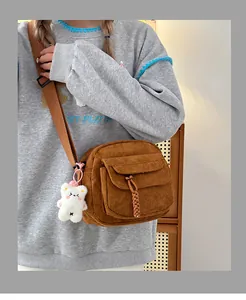 Detail of brown corduroy crossbody bag featuring a woven puller and plush bear charm
