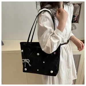 Detail of black tote bag with white pearls and rhinestone bow accessory on a model