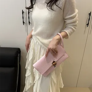 Pink lizard-embossed minimalist handbag with designer gold buckle held by a model