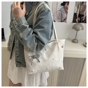 Close-up of white tote bag featuring elegant pearl accents and a rhinestone bow detail
