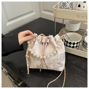 Detail of pink floral brocade bucket bag with pearl handle and chain strap on a desk