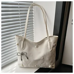 Detail of cream tote bag featuring pearls, a silver bow charm and pink heart gem