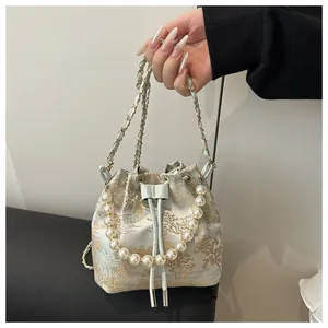 Close-up of landscape brocade fabric, pearl handle and chain strap on bucket bag