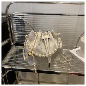Detail of satin bucket bag featuring floral embroidery, pearl handle, and gold chain strap
