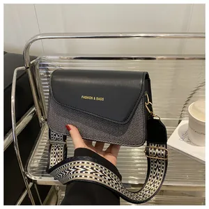 Close-up of contrast leather shoulder bag with gold lettering and geometric wide strap