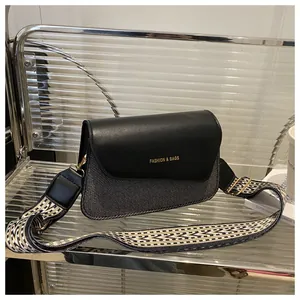 Detail of black leather square bag featuring a wide patterned strap on glass shelf