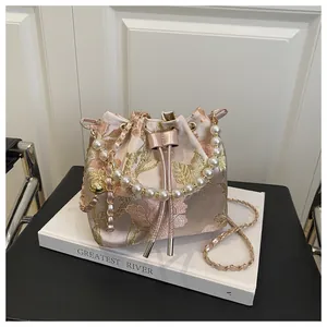 Detailed embroidery on champagne pink satin bucket bag with pearls and ribbon
