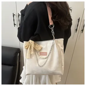 Close-up of a white tote bag featuring a pink shoulder strap, pearl chain, and lace bow detail