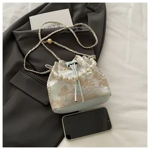 Close-up of mint green bucket bag featuring gold mountain embroidery and pearl handle