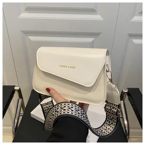 Detail of cream leather crossbody bag with wide geometric pattern strap and gold hardware