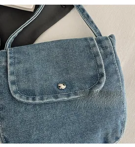 Close-up of blue denim shoulder bag featuring twill texture and silver metal buckle