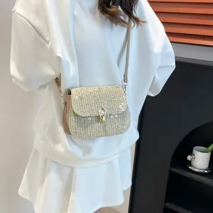Sac bandoulière en paille avec broderie florale et fermoir doré porté par un modèle