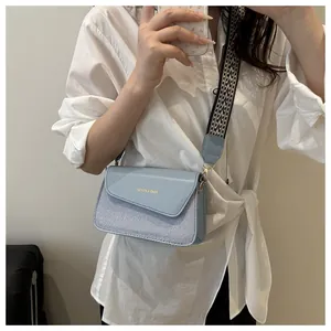 Detail of light blue crossbody bag with textured fabric, wide patterned strap and gold hardware
