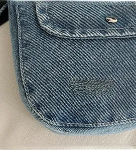 Close-up of blue denim texture with white contrast stitching and silver metal hardware