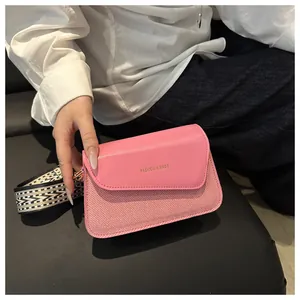 Detail view of pink leather crossbody bag with patterned wide shoulder strap and gold text