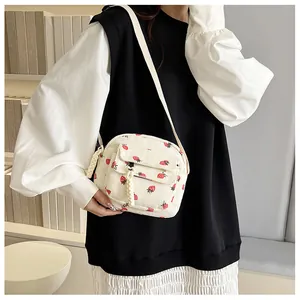 Detail of strawberry print corduroy crossbody bag with woven rope zipper pull decoration