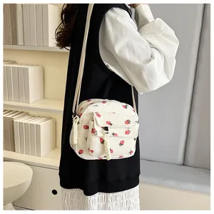 Detail view of white corduroy crossbody bag with cute red strawberry patterns and strap