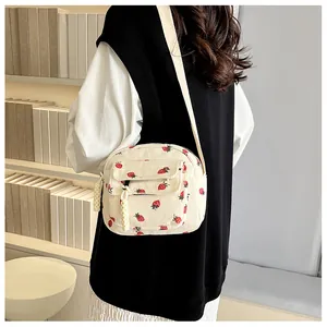 Detailed macro view of white corduroy strawberry print crossbody bag with woven zipper pull