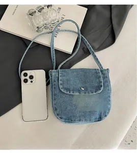 Detail view of mini denim crossbody bag with silver magnetic clasp next to a smartphone
