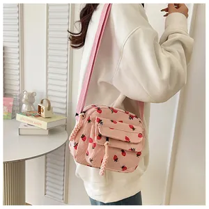 Detail of pink corduroy crossbody bag with strawberry print and woven zipper pull
