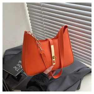 Vibrant orange hobo bag with gold metal latch and chain detail on a grey fabric