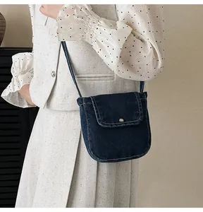 Detail of dark blue denim crossbody bag featuring contrast stitching and metal buckle