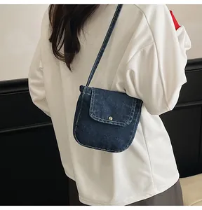 Detail of deep blue denim crossbody bag with white contrast stitching and minimalist flap