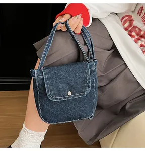 Detail of dark blue denim handbag with white contrast stitching and silver metal button