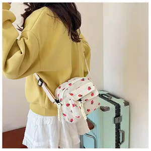 Detail of white corduroy crossbody bag with strawberry print and adjustable strap worn by model