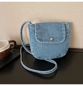 Close-up of blue denim crossbody bag with silver button closure and stitching detail