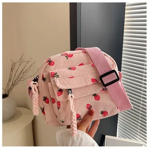 Detail of pink corduroy crossbody bag featuring strawberry prints and a woven pendant